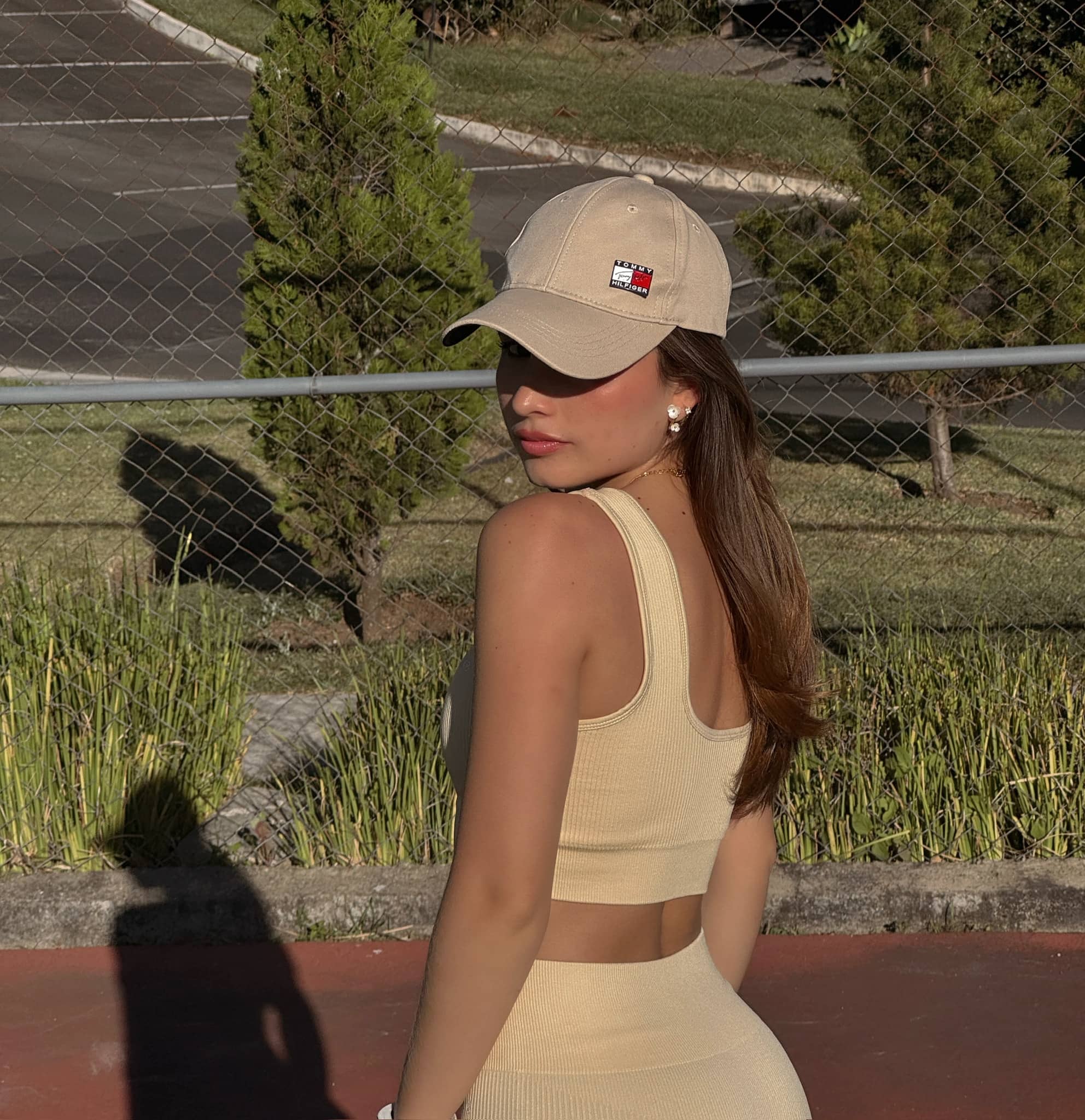 Modelo femenina usando un top de activewear color butter yellow sin mangas, de espaldas, en una cancha deportiva al aire libre.