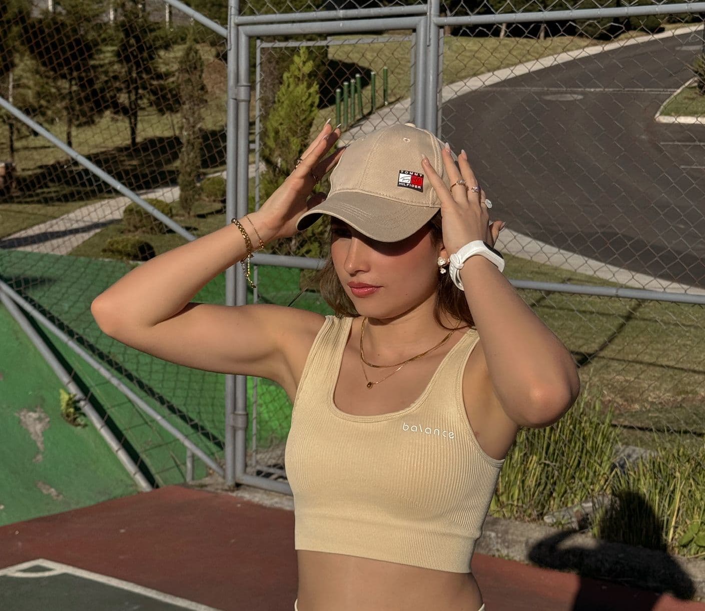 Modelo femenina de frente usando un top de activewear color butter yellow sin mangas, ajustándose una gorra en una cancha deportiva.